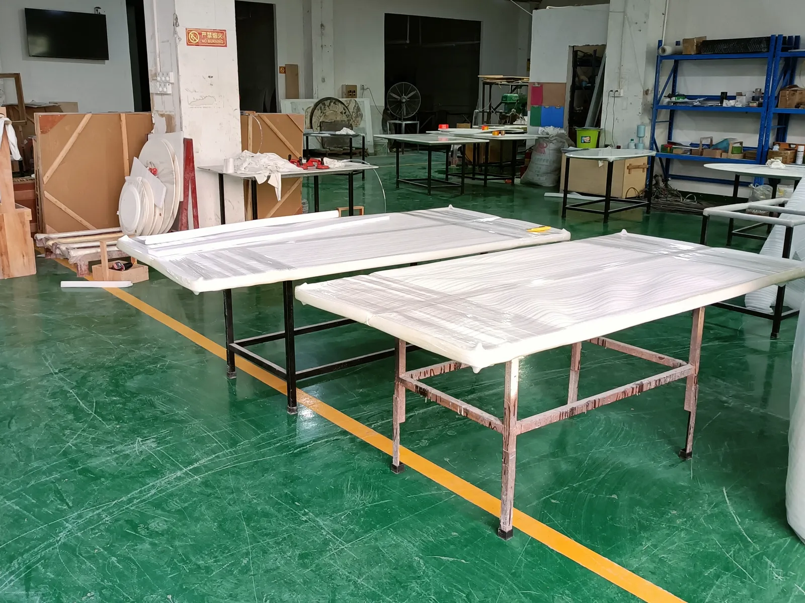 Film-wrapped table tops laid out on workbenches on a factory floor