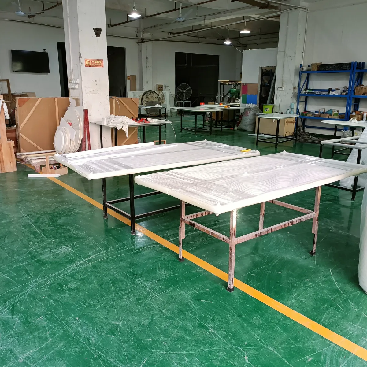 Film-wrapped table tops laid out on workbenches on a factory floor